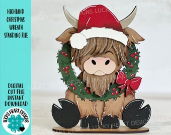 May include: A Highland cow Christmas decoration with a red Santa hat and a green wreath. The cow has brown fur and is sitting on a wooden base. The text "HIGHLAND CHRISTMAS WREATH STANDING FILE" is visible.