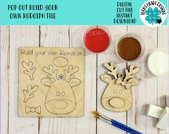 May include: A wooden craft kit for making a reindeer ornament. The kit includes a pre-cut reindeer head, antlers, and a bow tie. The kit also includes paint and paintbrushes. The text "Build your own Reindeer" is printed on the wood.