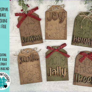 May include: Six wooden Christmas gift tags with different phrases. The tags are brown with white lettering and have red and white ribbon tied around them. The phrases are "Tis the season", "Joy to the world", "Merry and bright", "Santa Stop Here", "Holly Jolly", and "Farm Fresh Trees".