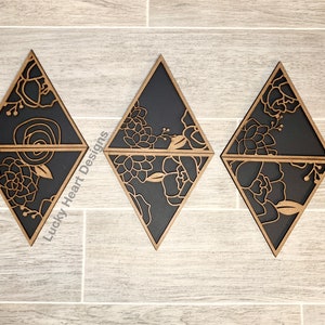 May include: Three black diamond-shaped wooden wall decor pieces with a floral design cut out. The floral design is in a light brown color. The text "Lucky Heart Designs" is visible in the image.