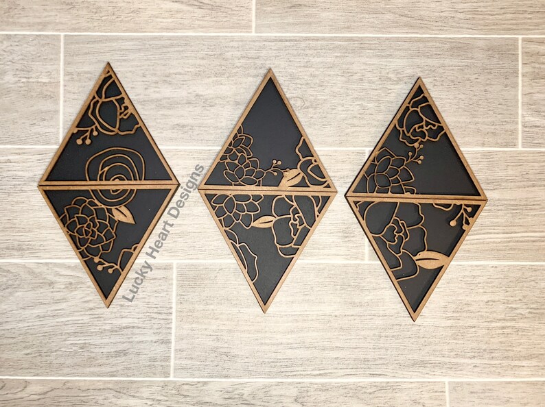 May include: Three black diamond-shaped wooden wall decor pieces with a floral design cut out. The floral design is in a light brown color. The text "Lucky Heart Designs" is visible in the image.