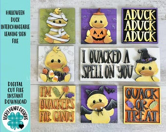 May include: A collection of Halloween-themed wooden signs featuring duck characters in various costumes. The signs include phrases like "Aduck," "Quack or Treat," and "I Quacked a Spell on You." The signs are square and have a rustic, handcrafted appearance.
