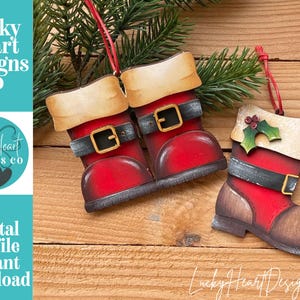 May include: Two hanging ornaments shaped like Santa boots. One ornament features a pair of red boots with black belts, gold buckles, and cream-colored cuffs. The second ornament is a single red boot with a black belt, gold buckle, and a holly leaf accent.