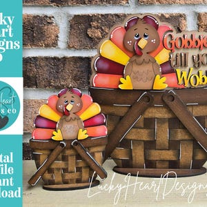 May include: Thanksgiving-themed wooden decorations featuring cartoon turkeys in baskets. The turkeys have colorful tail feathers and are perched on brown baskets. One sign reads "Gobble till you Wobble". The image includes the text "Lucky Heart Designs Co."