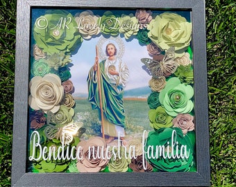 May include: A framed shadow box with a religious image of Saint Joseph, surrounded by green and brown paper flowers. The text "Bendite nuestra familia" is written in white on the bottom of the frame.