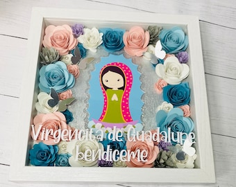 May include: A white frame with a silver background and a paper flower arrangement. The flowers are in shades of pink, blue, and white. The center of the frame features a cartoon image of the Virgin Mary with the text "Virgencita de Guadalupe Bendiceme".
