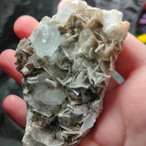 Op de afbeelding: Een natuurlijk mineraal specimen met een cluster van lichtbruine, gelaagde kristallen met ingebedde, doorschijnende, lichtblauwe kristallen. Het mineraal heeft een ruw, getextureerd oppervlak.