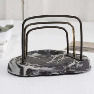 May include: A black and white marbled ceramic napkin holder with a gold and black metal frame.