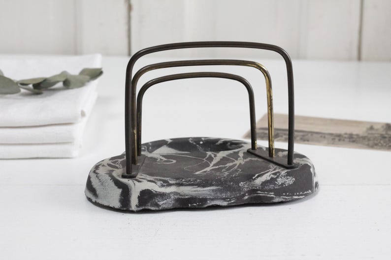 May include: A black and white marbled ceramic napkin holder with a gold and black metal frame.