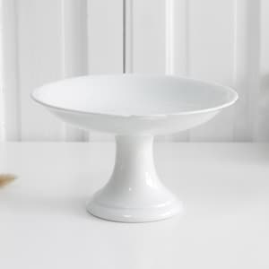 Pode incluir: Uma taça de cerâmica branca sobre pedestal com uma bacia larga e rasa, acabamento liso e brilhante e uma base robusta e alargada. O design é simples e funcional, com uma cor branca uniforme em toda a estrutura da peça.