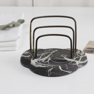 May include: A black and white marble letter holder with a gold metal frame. The frame has three horizontal bars.
