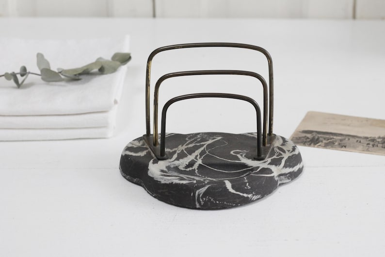 May include: A black and white marble letter holder with a gold metal frame. The frame has three horizontal bars.