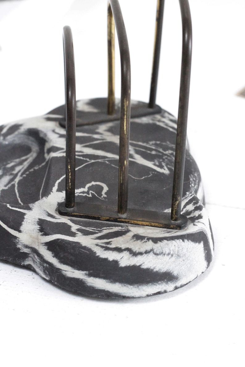 May include: Black and white marbled paperweight with a metal letter holder on top. The letter holder has three vertical bars.