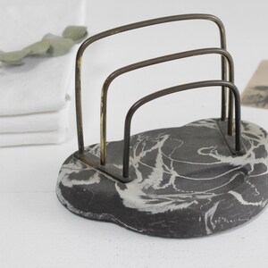 May include: A black and white marbled stone letter holder with a brass wire frame. The letter holder has three compartments.
