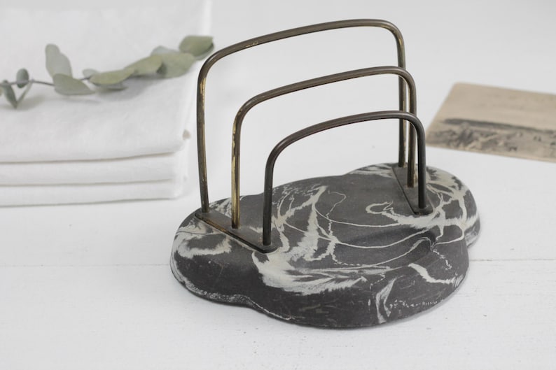 May include: A black and white marbled stone letter holder with a brass wire frame. The letter holder has three compartments.