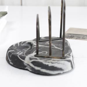 May include: Black and white marble napkin holder with a metal frame. The holder has a modern design and is perfect for holding napkins or other small items.