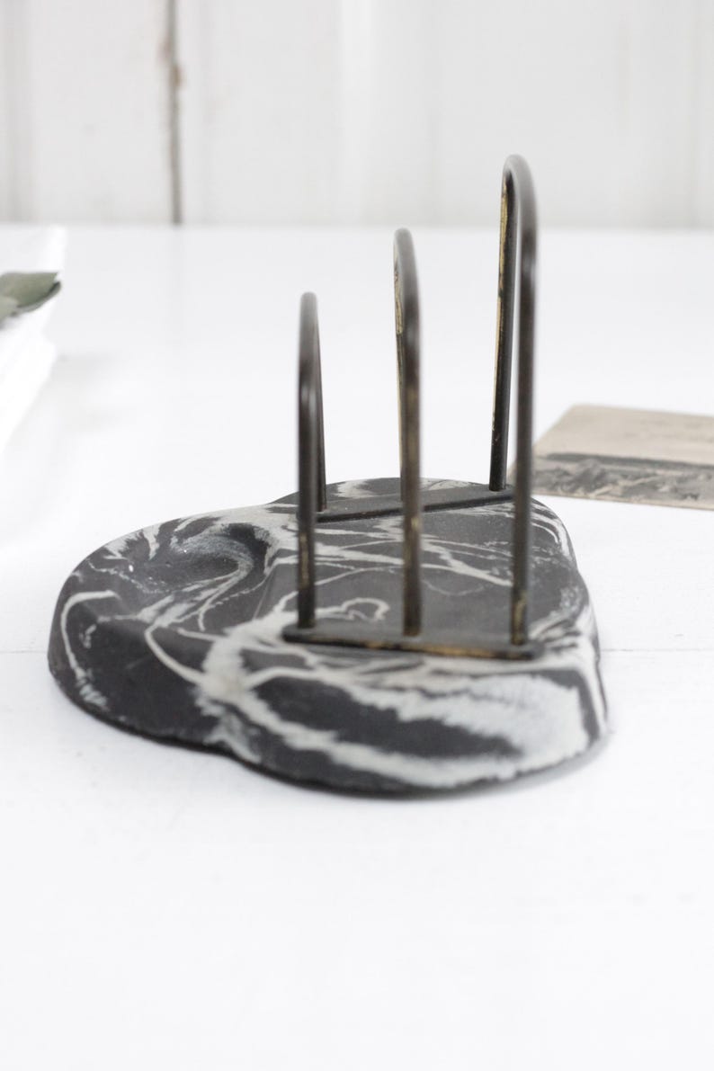 May include: Black and white marble napkin holder with a metal frame. The holder has a modern design and is perfect for holding napkins or other small items.