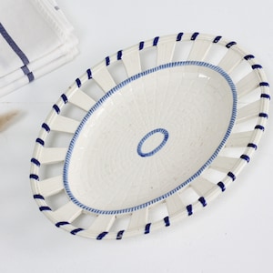 May include: White oval ceramic serving dish with a blue and white trim. The dish has a woven pattern and a cut-out design around the edge.