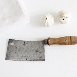 May include: A vintage cleaver with a wooden handle and a metal blade. The blade is dull and has a few scratches. The handle is brown and has a few knots in the wood.