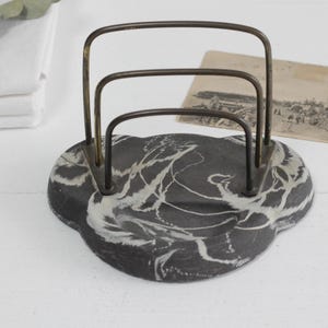 May include: A black and white marbled letter holder with a brass wire frame. The letter holder has three compartments for holding letters or papers.