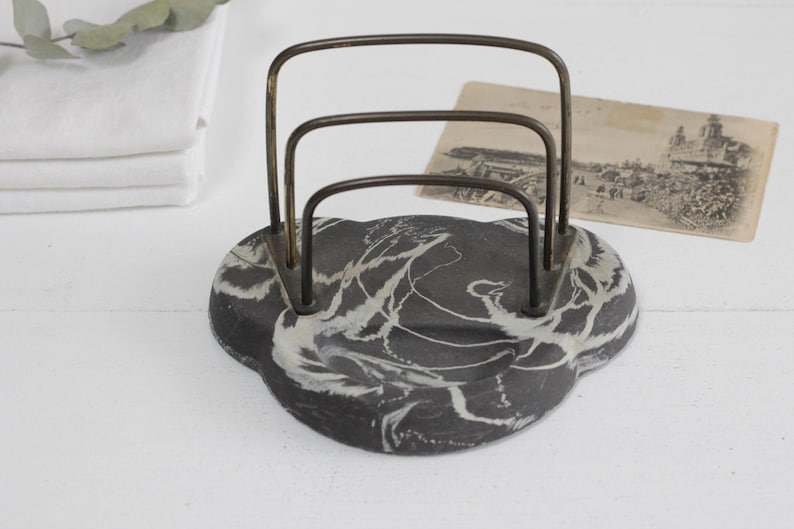 May include: A black and white marbled letter holder with a brass wire frame. The letter holder has three compartments for holding letters or papers.