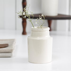 May include: A white ceramic vase with a small bouquet of white flowers.