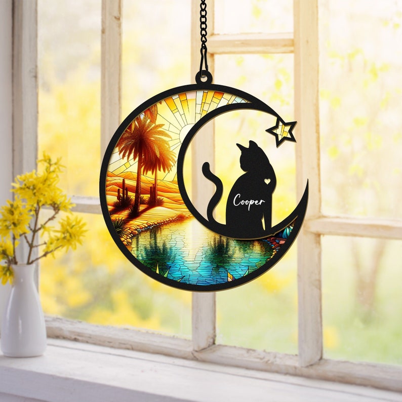 May include: A black metal moon-shaped wind chime with a stained glass design of a desert scene and a cat silhouette. The cat silhouette has the name "Cooper" written on it.