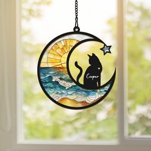 May include: A stained glass sun and moon window hanging with a black silhouette of a cat and the name "Cooper" written on the moon.