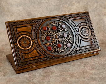 May include: A wooden game board with intricate carvings of a pomegranate tree and other floral designs. The board is closed and has a hinged lid.