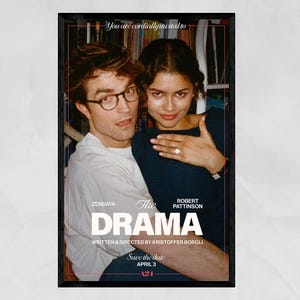 May include: A framed movie poster featuring Zendaya and Robert Pattinson. The title "The Drama" is prominently displayed, with the text "Save the date APRIL 3" below. The actors are embracing, with a bookshelf visible in the background.