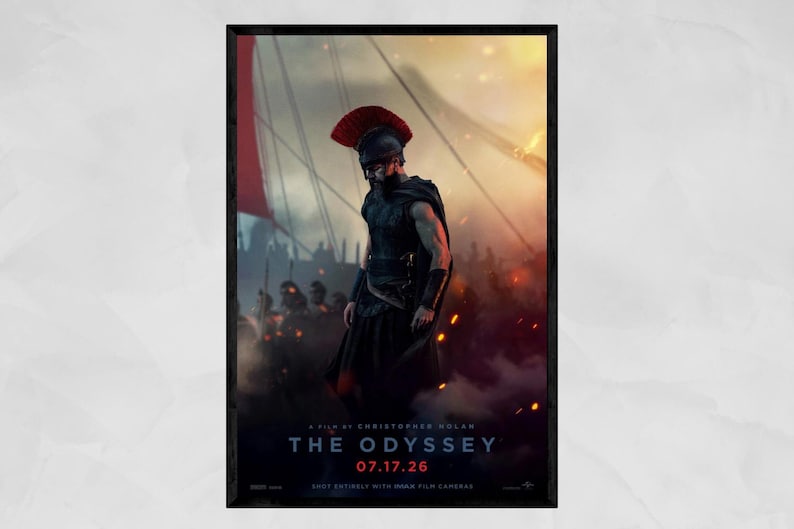 May include: A movie poster for The Odyssey, directed by Christopher Nolan, featuring a warrior in a dark helmet with a red crest and black armor. The scene shows a battlefield with ships and fire, with the text 07.17.26 displayed in red.