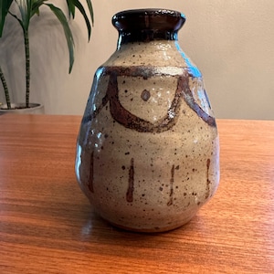 May include: A ceramic vase with a brown and white speckled glaze. The vase has a brown rim and a geometric design in brown and white.