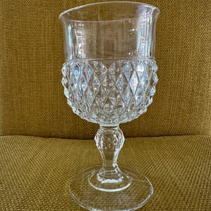 May include: A clear glass goblet with a diamond-shaped pattern. The goblet has a tall, slender stem and a wide, round base.
