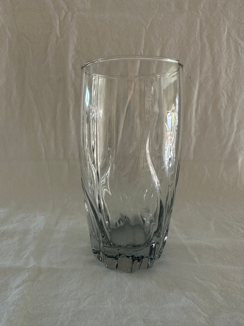 May include: A clear glass drinking glass with a textured, wavy design. The glass has a wide base and a slightly flared top.