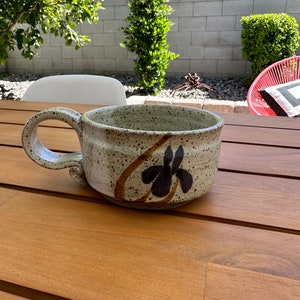 May include: A speckled brown ceramic mug with a black and brown floral design and a large handle.