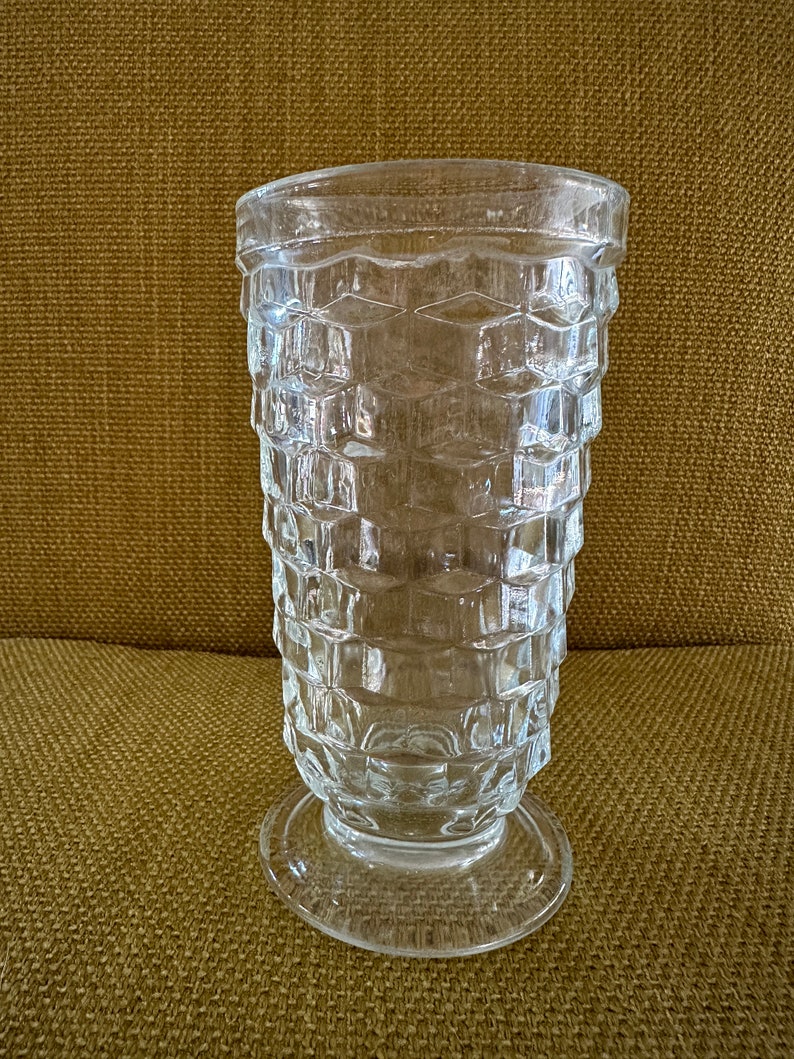 May include: A clear glass vase with a textured, diamond-shaped pattern. The vase has a wide base and a narrow opening.