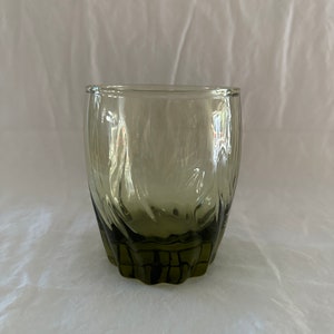 May include: A dark green glass tumbler with a textured, wavy design. The glass has a rounded bottom and a wide mouth.