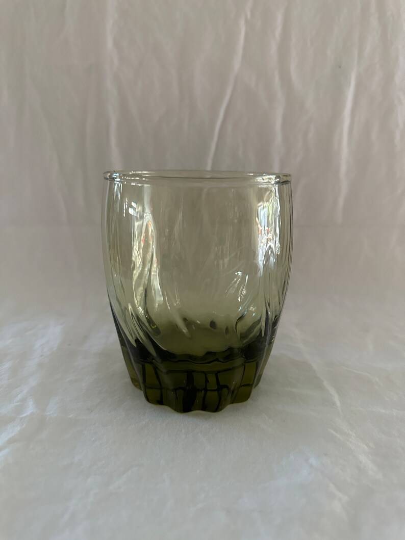 May include: A dark green glass tumbler with a textured, wavy design. The glass has a rounded bottom and a wide mouth.