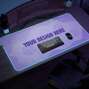 May include: A rectangular, purple gaming mouse mat with a glowing blue edge. The mat features paw prints and the text "YOUR DESIGN HERE". A black keyboard and mouse sit on the mat. A curved monitor is in the background.