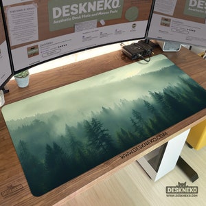 May include: A rectangular desk mat featuring a forest scene. The design depicts a misty forest with tall green trees. The mat has the text "DESKNEKO" and "Aesthetic Desk Mats and Mouse Pads" printed on it.