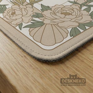 May include: A beige and white floral mousepad featuring a peony design with green leaves. The mousepad has a stitched edge and a beige border. The Deskneko logo and website address are visible in the bottom right corner.