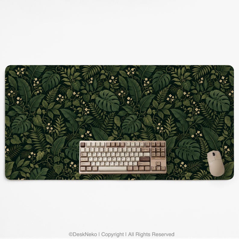 K&ouml;nnte beinhalten: Eine rechteckige Schreibtischunterlage mit einem dichten, dunkelgr&uuml;nen botanischen Muster aus Monstera-Bl&auml;ttern, Farnen und kleinen wei&szlig;en Bl&uuml;ten. Eine beige mechanische Tastatur und eine passende beige Computermaus liegen auf der Unterlage.