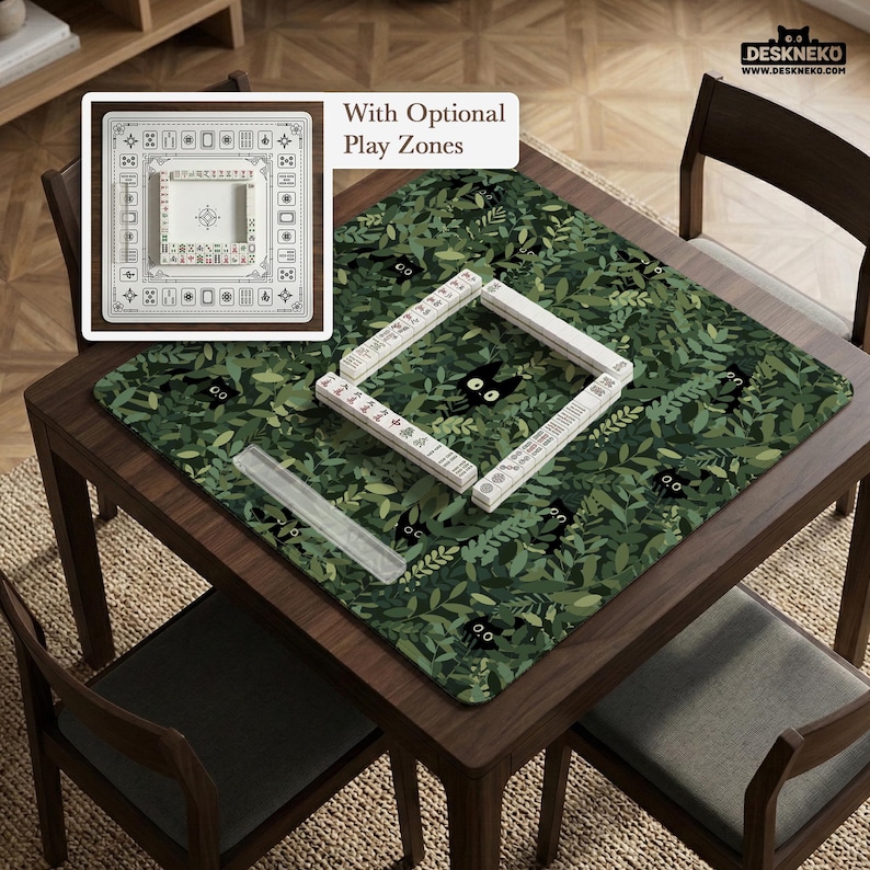 May include: A wooden table with a green leaf-patterned mat featuring black cat illustrations. White Mahjong tiles are arranged on the mat. A white square game board with optional play zones is in the upper left corner. The table is surrounded by wooden chairs.
