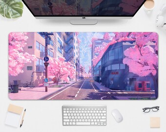May include: A rectangular desk mat featuring a vibrant anime-style illustration of a street lined with pink cherry blossom trees. Buildings and a road are in the center, with a blue sky peeking through the trees. A keyboard, mouse, and monitor are visible.