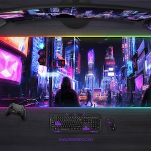 Op de afbeelding: Een groot rechthoekig gaming muismat met een levendig stadsgezichtontwerp, verlicht door een kleurrijke LED-rand. De mat heeft een toetsenbord, muis en controller, met het websiteadres www.deskneko.com zichtbaar.