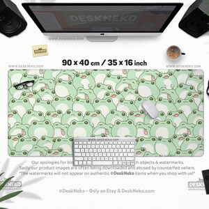 May include: A large desk mat featuring a repeating pattern of light green cartoon frogs. The mat measures 35 x 16 inches and has a white keyboard, mouse, and glasses on top. The text "DeskNeko" and website address are visible.