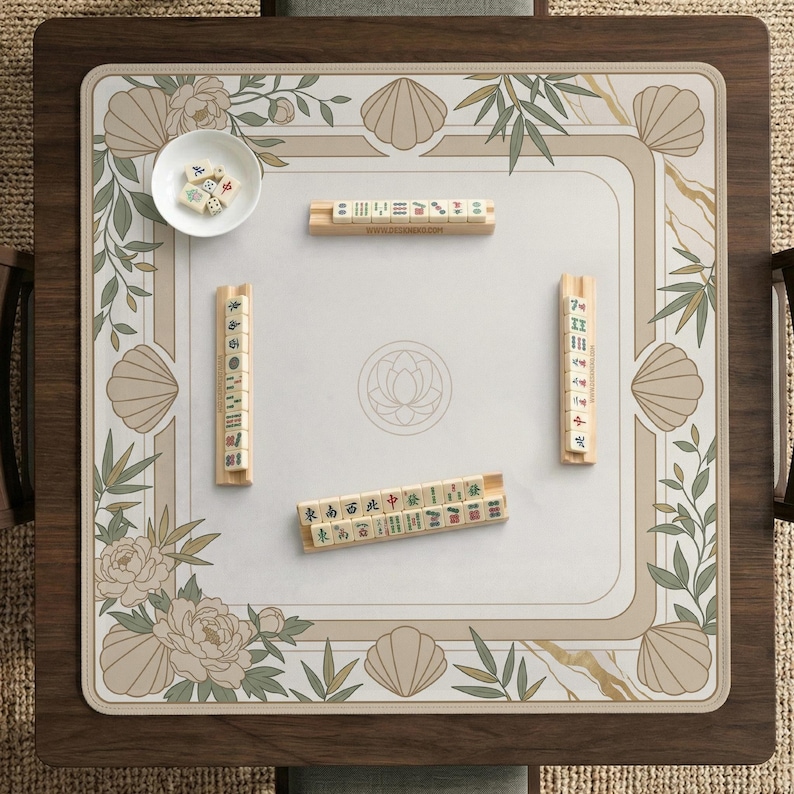 May include: A wooden Mahjong game set with a floral and seashell design. The set includes a playing surface, tiles, and dice. The playing surface is beige with a floral and seashell border. The tiles are beige with black and green markings.