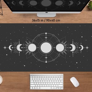 May include: A black desk mat with a celestial design featuring moons, suns, and stars. The mat measures 36x15 inches. The design is in white and gray, set against a dark background. A keyboard, mouse, and monitor are visible.
