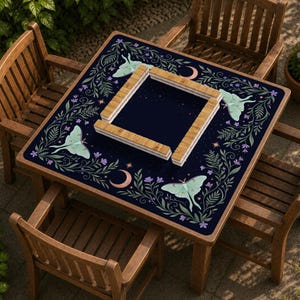 Può includere: Un tappetino quadrato per tavolo da mahjong con sfondo blu scuro e un bordo botanico di foglie verdi, fiori viola e falene luna verde chiaro. Il tappetino presenta mezzelune e stelle color rame, con una cornice in legno per le tessere.