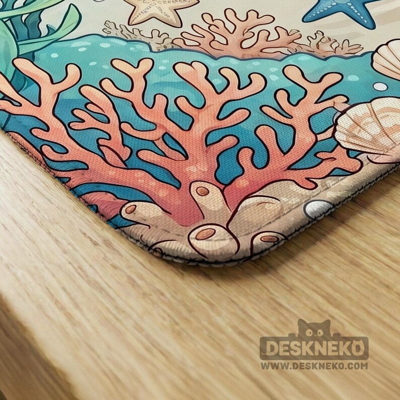May include: A colorful desk mat featuring an underwater scene with coral, starfish, and seashells. The design includes shades of blue, pink, and beige, creating a vibrant and playful aesthetic. The mat has a black border and the text "DESKNEKO WWW.DESKNEKO.COM".